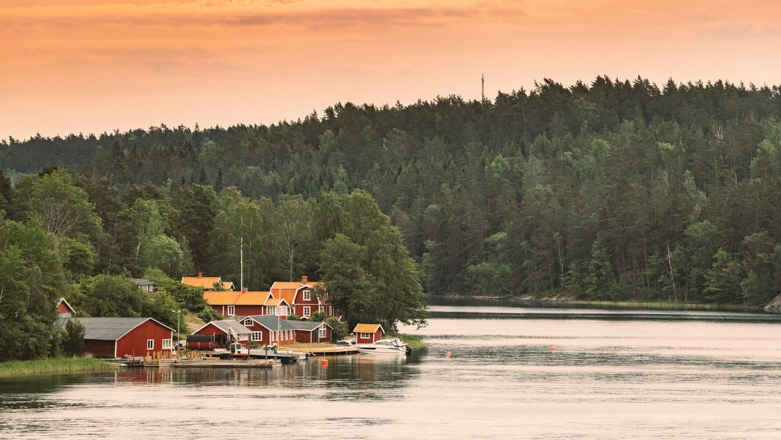 Sweden. Many Beautiful Red Swedish Wooden Log Cabins Houses On Rocky Island Coast. Lake Or River Landscape Туры по Швеции с IBG Travel